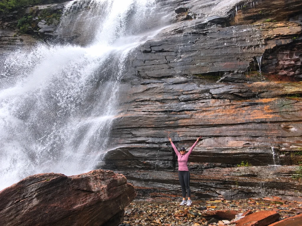 Thais Campos de braços abertos diante de uma cachoeira que desce pela rocha, em Telluride.