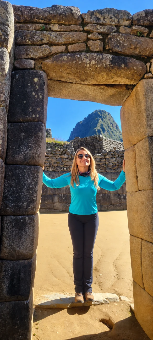 Thais Campos sorrindo sob uma porta de pedra em Machu Picchu, com a montanha ao fundo.